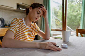 Naklejka premium Thoughtful woman indoors, resting hand on her forehead at home desk with notebook and mug, daytime light, striped shirt, reflective mood, casual lifestyle, focused moment