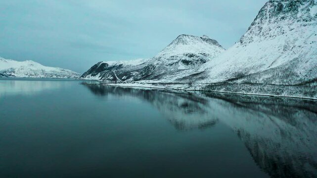 Drohnenflug &uuml;ber Fjord mit verschneiten Bergen in Nordnorwegen