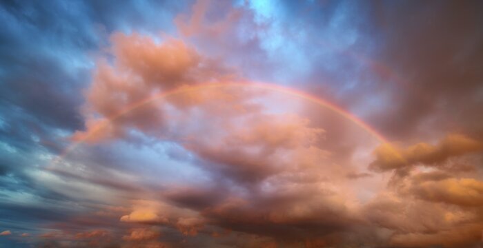 Rainbow in atmospheric sky with storm clouds at sunset