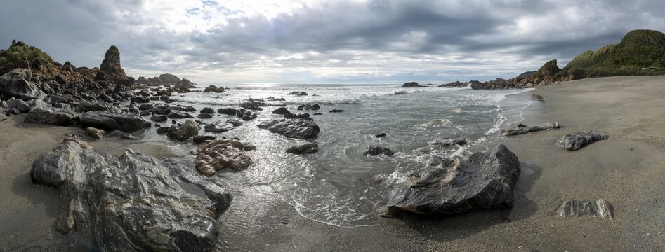 Rocky coast, rocks on the beach, dark rain clouds, long time exposure, West Coast, South Island, New Zealand