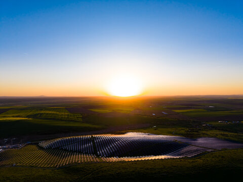 Sunrise over solar panels in a rural area with fields and hills in the background capturing the early morning light and changing colors of the sky
