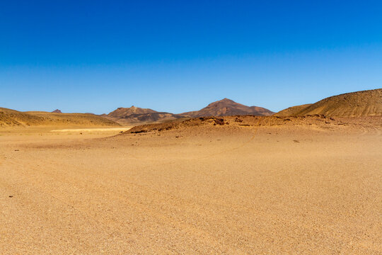The Sahara Desert. A serir-type desert.  Flat, gravelly  desert terrain. The Tadrad Rouge mountains in the background. Algeria, Africa