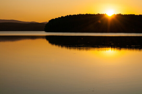 Panoramic summer solstice landscape, the sun setting behing the trees at the lake lit by golden sunset light, summer time background, golden hour at the nature