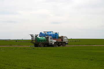 Fototapeta premium Treating winter wheat seedlings with pesticide. A self-propelled sprayer and a tanker truck in the field.