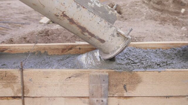 Construction worker actively pouring concrete into forms. Construction worker skillfully pouring wet concrete into formwork amid surrounding earth and safety gear