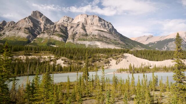 Turquoise alpine lake below towering peaks, evergreen forest foreground, jagged limestone mountains, soft cloud shadows, glacial sediment shorelines, tranquil reflections, Canada