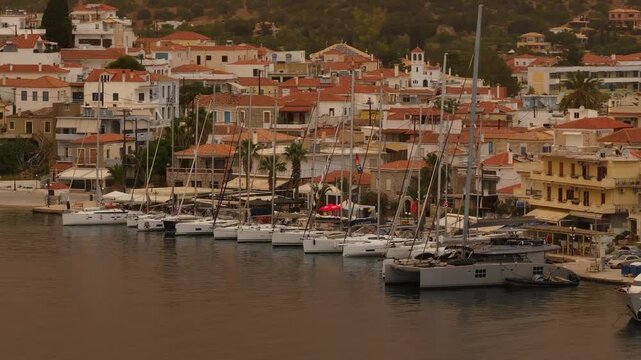 Aerial telephoto drone orbit from left to right along sailing yachts moored in Ermioni harbor with cinematic Mediterranean atmosphere and orange sky