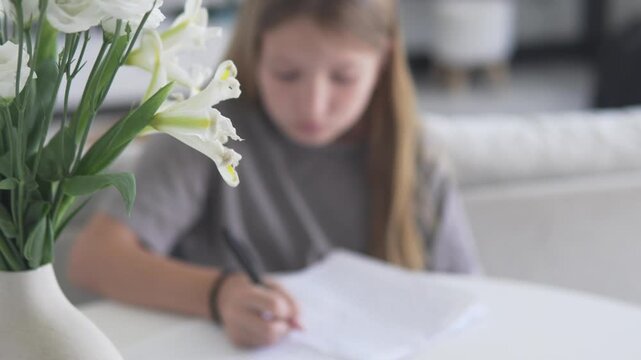 Focus on flowers, in the background a girl writes handwriting at home