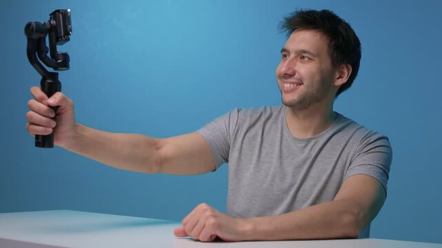 Person adjusts camera stabilizer while smiling in professional studio setup. Person in casual attire is testing camera movement techniques in blue studio environment