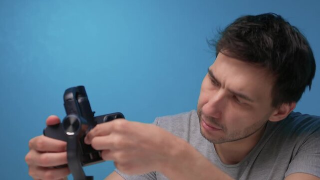 Person adjusts camera stabilizer while smiling in professional studio setup. Person in casual attire is testing camera movement techniques in blue studio environment