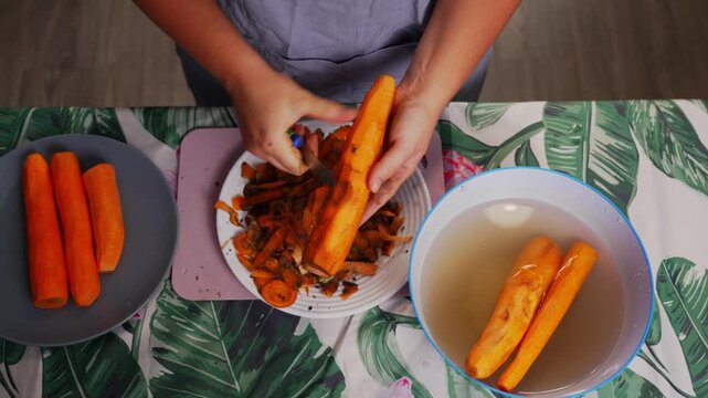 Close up of female hands peeling fresh carrot with knife during vegetable preparation for homemade cooking in kitchen with healthy natural ingredients. High quality 4k footage