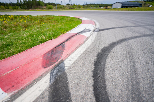 Sharp turn on a professional asphalt race track with red and white striped rumble strips and visible black tire skid marks indicating high speed drifting and motor sports