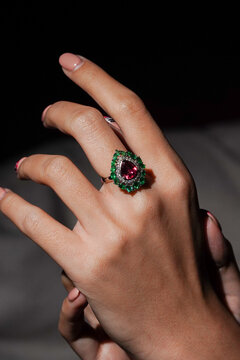 Hand wearing a pear-shaped ruby and an emerald ring