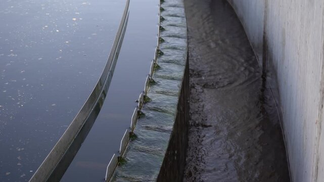 Close-up of water flowing over a V-notch weir in a clarifier tank at a wastewater treatment facility. Ideal B-roll for projects on ESG, sustainable infrastructure, and water purification.