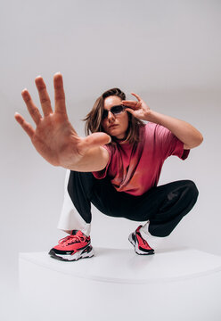 Emotional female hip hop dancer posing and dancing on a gray studio background. Dynamic wide-angle shot with joy, laughter, and urban street style