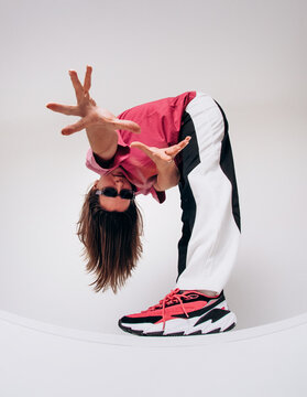 Emotional female hip hop dancer posing and dancing on a gray studio background. Dynamic wide-angle shot with joy, laughter, and urban street style