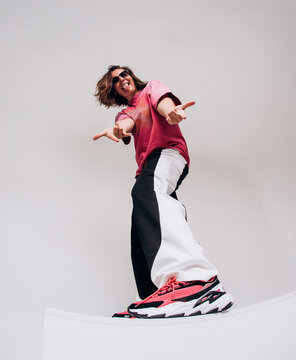 Emotional female hip hop dancer posing and dancing on a gray studio background. Dynamic wide-angle shot with joy, laughter, and urban street style