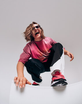 Emotional female hip hop dancer posing and dancing on a gray studio background. Dynamic wide-angle shot with joy, laughter, and urban street style