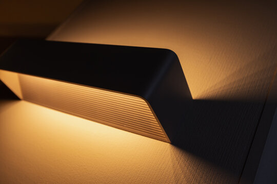 A warm modern wall sconce emits soft ambient light, casting dramatic shadows that emphasize the textured interior wall; minimalist lighting and sleek design, cozy contemporary architectural mood