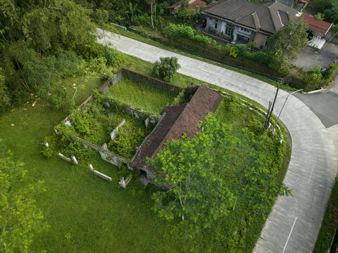 Aerial view of houses damaged by Mount Merapi eruption overgrown with lush vegetation and abandoned stone walls near a paved road in Cangkringan, Special Region of Yogyakarta, Indonesia.