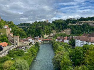 Fototapeta premium Scenic view of the Sarine river winding through the historic old town of Fribourg, Switzerland under a dramatic sky.