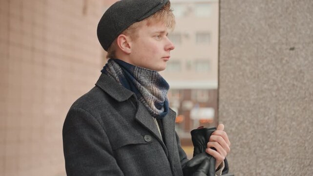 Young white creator scouting urban location beretwearing director studies light and framing with camera in hand city balcony background quiet overcast morning focused creative planning