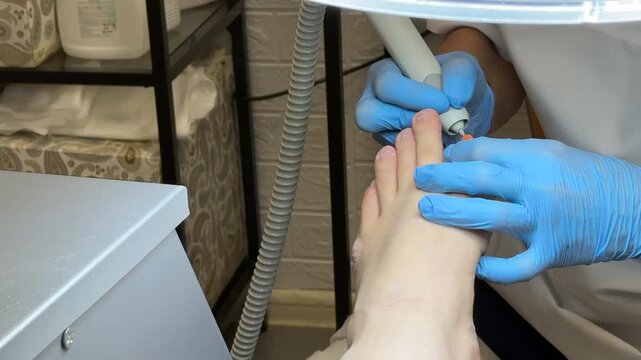 Close-up man foot pedicure diamond drill master wearing blue gloves working on toenail electric file smoothing callus salon lamp