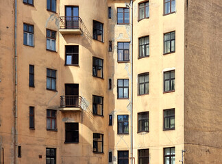 Fototapeta premium Weathered yellow stucco facade of an old residential apartment building with windows and balconies; typical Eastern European or Baltic urban architecture and housing infrastructure