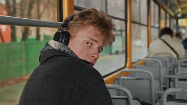 Caucasian creator turns toward camera midride glance across empty seats, observing urban street, scouting vlogger shots, subtle curiosity, green construction fence outside, cold season, candid
