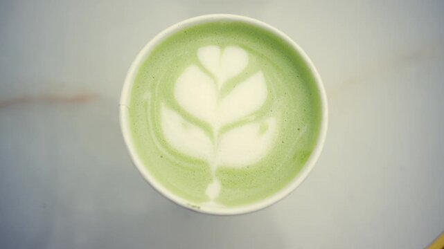 Top down view of a green matcha latte with detailed leaf shaped latte art made from steamed milk