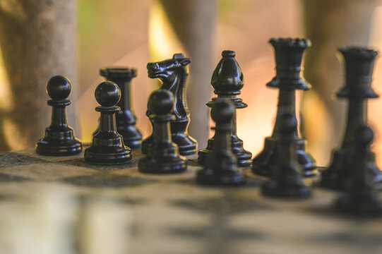 Close up of black chess pieces on rustic outdoor board with shallow depth of field.