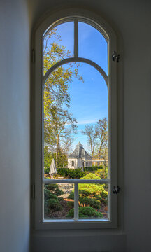 View through arched window onto garden pavilion and manicured landscape outside.