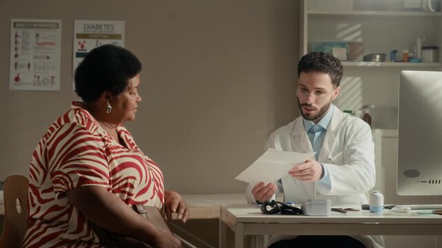 Medium shot of Middle Eastern male doctor handing recommendation paper to senior Black female patient with diabetes thanking him after medical appointment in modern clinic