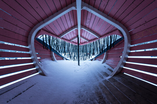 Heart shaped wooden shelter interior with snow covered floor in winter park landscape.