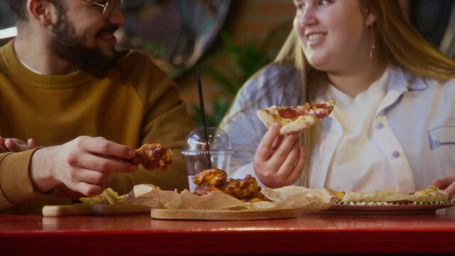 Low angle shot of young beared biracial man having coversation and enjoying fast food with woman in cafe