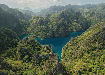 Fototapeta premium Panoramic aerial drone view of Twin Lagoon in Coron, Philippines, showcasing dramatic limestone karst mountains, tropical forest and deep turquoise waters surrounded by the breathtaking landscape
