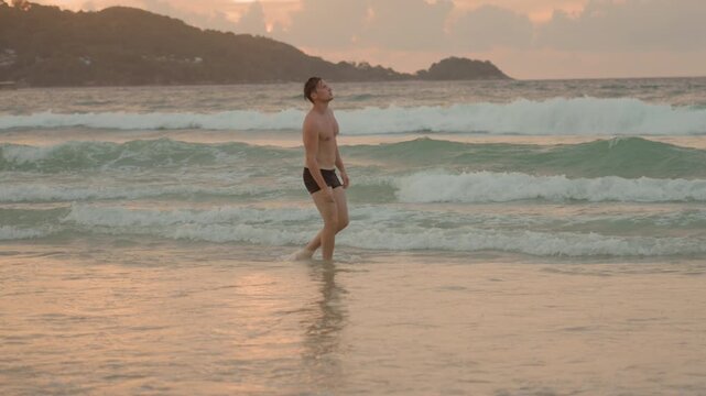 Caucasian man exploring coastal shoreline. Sunset walk with footprints and lively ocean waves after daylight. Casual evening walk along coast with wet footprints and warm sunset glow
