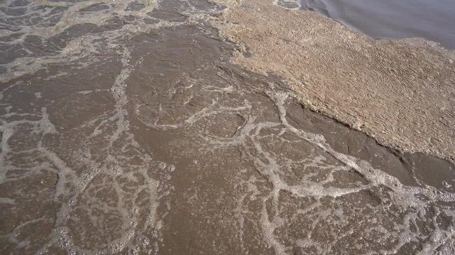 Extreme close-up of churning foam and activated sludge in a wastewater treatment aeration tank. Essential B-roll illustrating water pollution, biological sewage treatment, and ESG infrastructure.