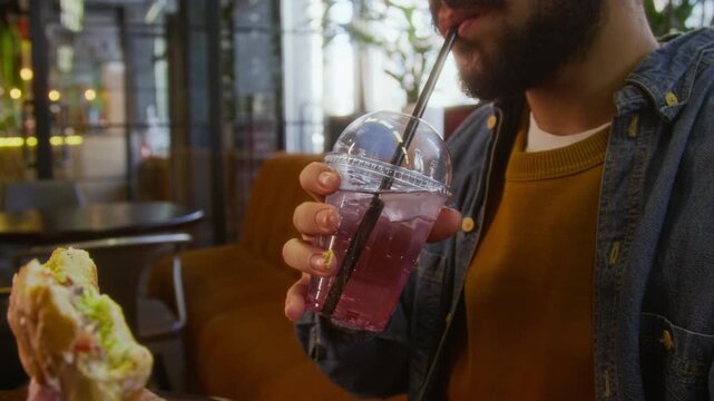 Close up low angle shot of unrecognizable bearded man sipping drink and enjoying cheeseburger at restaurant