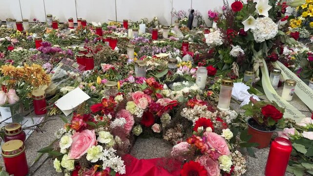 Public memorial with flowers and candles placed along a wall in remembrance of victims after a tragic event. Symbol of mourning, condolences, grief, solidarity and collective tribute.