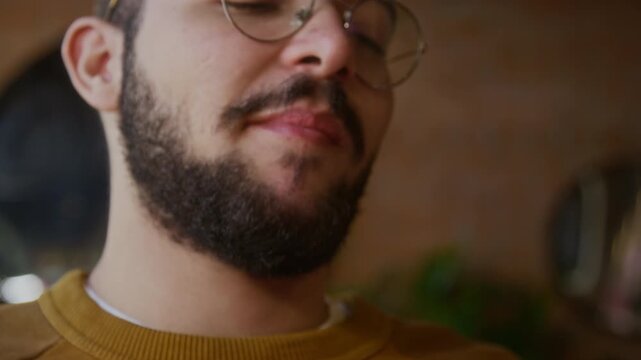 Close up low angle shot of young biracial man with beard and glasses sipping drink and enjoying chicken wings in fast food cafe