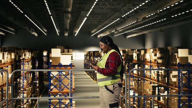 Black call center agent using headset to provide tracking info and shipment updates. Worker monitoring airway bill numbers, parcel barcodes and order status, express delivery in fulfillment center.