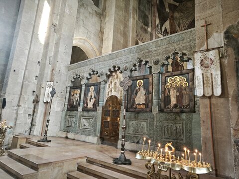Ornate stone iconostasis with painted religious icons inside a historic church. Orthodox altar screen with burning candles in the foreground