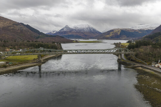 Aerial view of Ballachulish Bridge spanning Loch Leven with snow-capped mountains and a cloudy sky in the background Ballachulish, Scotland, United Kingdom.