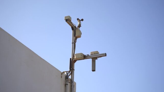 Close-up of an anemometer spinning in the wind against a blue sky on an industrial building. Essential B-roll for meteorology, environmental monitoring, climate change, and ESG infrastructure projects