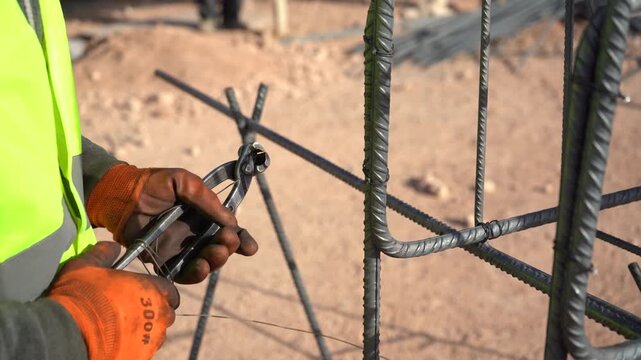 Close-up of a construction worker's gloved hands tying steel rebar with wire and pliers. Essential B-roll highlighting skilled manual labor, civil engineering, and concrete foundation preparation.