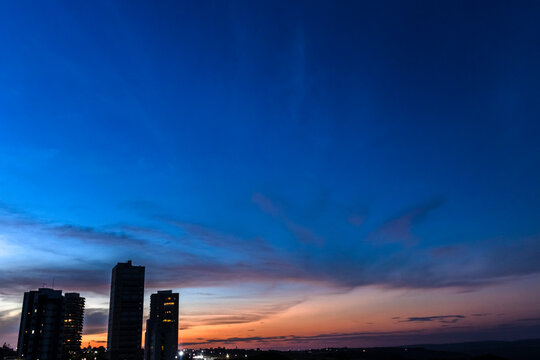 Modern urban skyline silhouette under a dramatic twilight sky. A panoramic view of high-rise buildings contrasting against a vibrant blue and orange horizon. 
