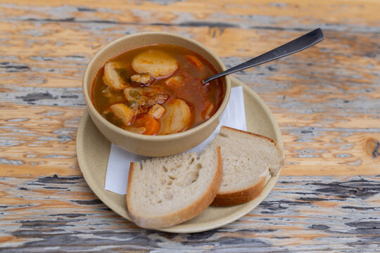 Hearty soup with vegetables and potatoes in a bowl. Served with sliced bread on a rustic wooden table. Simple meal presented on a warm, natural surface. Cozy, inviting, comforting food for a quiet day