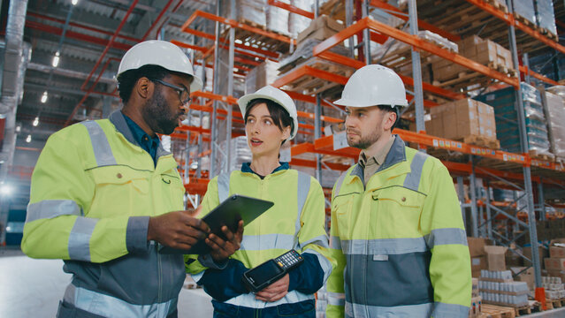 African American male worker explaining task and using tablet device. Working in warehouse. Serious woman holding barcode scanner. Bearded man listening closely. Reviewing plan or shift goals.