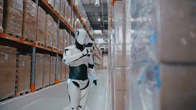 Futuristic robot scanning barcode on stacked boxes with handheld reader inside warehouse. Identifying inventory or updating database while assisting automated stock control in logistics environment.